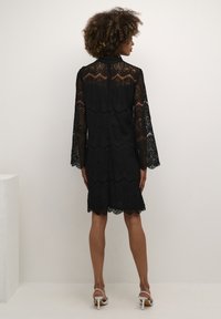 Black lace dress with long bell sleeves and a scalloped hem. Features intricate floral patterns and a high neckline.