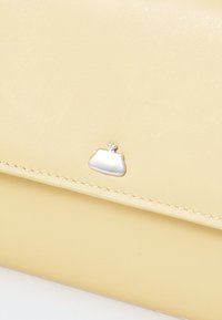 Cartera amarilla de cuero con costuras claras y un pequeño acento de cierre de plata. Textura suave, forma rectangular compacta.