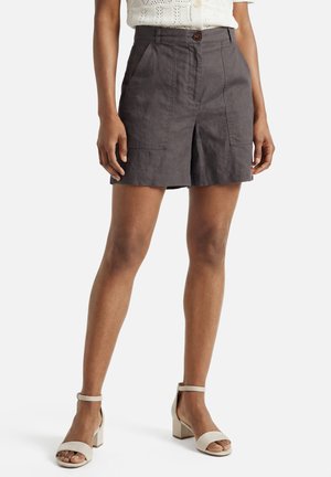 Femme portant un short taille haute gris foncé avec poches avant, associé à des sandales blanches à talons et un haut en maille blanc.