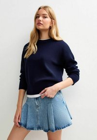 Maglione lavorato a maglia blu navy con spalle scese e polsini a costine, abbinato a una mini gonna plissettata in denim azzurro chiaro con tasche anteriori.