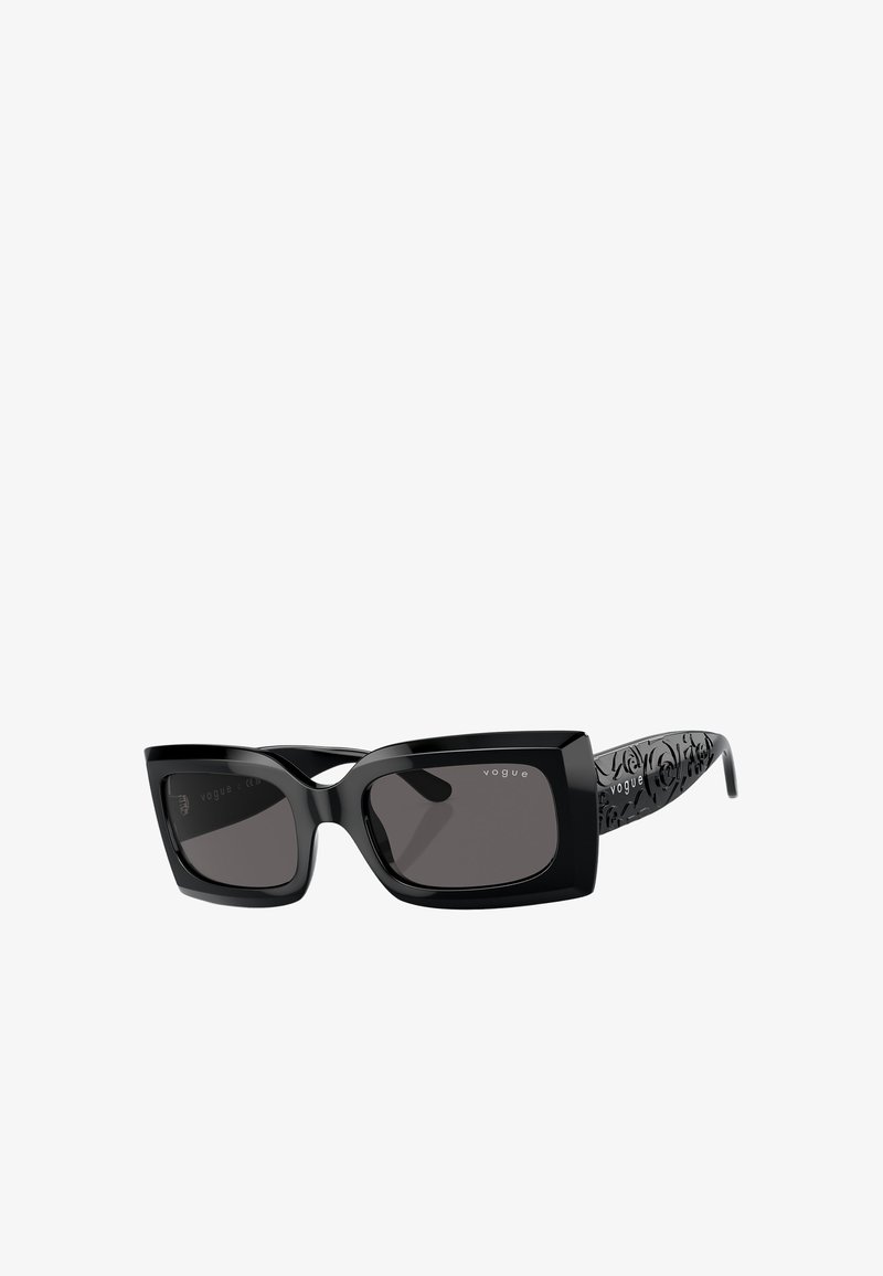 Occhiali da sole neri rettangolari con lenti scure. Presentano una forma unica a occhio di gatto e temple decorati con un motivo nero. Logo sulla lente destra.