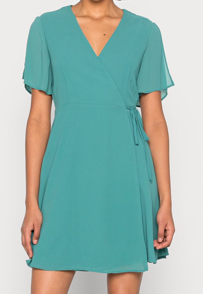 Robe portefeuille teal en tissu léger, avec des manches courtes à volants, un décolleté en V et un lien à nouer à la taille en croix pour un ajustement.