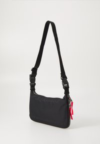 Black nylon shoulder bag with a zip closure, adjustable strap, and textured surface; features a red fabric tag and embossed text.