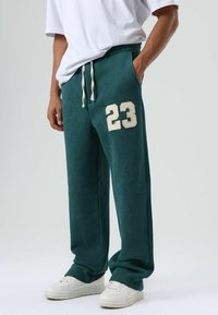 Turquoise joggingbroek met wit trekkoortje en geborduurd nummer "23" op het linkerbeen. Gecombineerd met witte sneakers. Zachte stof en losse pasvorm.