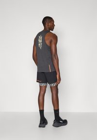 Μαύρο μπλουζάκι χωρίς μανίκια με ελαφρύ σχέδιο στην πλάτη, συνδυασμένο με μαύρες βερμούδες που διαθέτουν σχέδιο στο εσωτερικό και πορτοκαλί λεπτομέρειες. Μαύρα παπούτσια και κάλτσες.