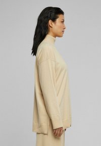 Beige turtleneck neule paita, jossa on rento istuvuus, pitkät hihat, joustavat hihansuut ja suora helma. Pehmeä kangas, minimaalinen muotoilu.