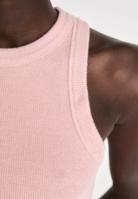 Pink sleeveless top made of textured fabric, featuring a high neckline and smooth, rounded armholes for ease of movement.