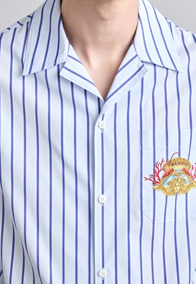 Light blue short-sleeve shirt with thin vertical stripes in darker blue. Features a chest pocket with a colorful graphic design.