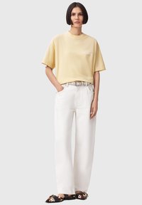 Κίτρινη υπερμέγεθη κοντομάνικη, άσπρο παντελόνι ψηλόμεσο με φαρδιά μπατζάκια και παπούτσια τύπου slip-on με σχέδια. Λείο ύφασμα, άνετη εφαρμογή.