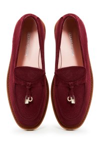 Bordeaux loafers i ruskind med en flad brun sål, der har en dekorativ snørelukning og en lille metalaccent foran.