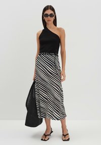 Top nero a spalla con una gonna midi a righe bianco e nere. Sandali neri e una borsa a tracolla nera con texture completano il look.