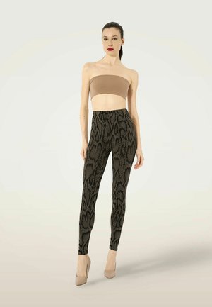 Vrouw met donker haar in een paardenstaart draagt een beige strapless crop top, slangenprint leggings en beige hoge hakken, staand tegen een effen achtergrond.