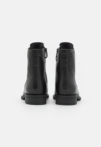 Bottines noires en cuir avec une surface texturée, un petit talon empilé et des zips sur le côté, présentant des détails de couture minimalistes.