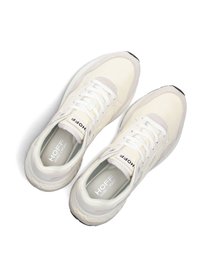 White sneakers with a mix of smooth and textured fabrics, featuring laces, a logo on the tongue, and a black rubber sole.