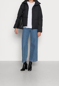 Person wearing black puffer jacket, white t-shirt, wide-leg blue jeans, black heeled boots, and carrying a large black shoulder bag.