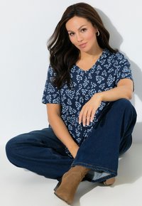 Granatowa bluzka z krótkim rękawem ozdobiona kwiatowym wzorem, z dekoltem w kształcie litery V. Do tego ciemnoniebieskie, szerokie dżinsy oraz brązowe botki za kostkę.