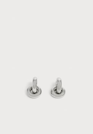 Paire de petites boucles d'oreilles créoles argentées brillantes avec une base ronde, présentées sur un fond clair uni.