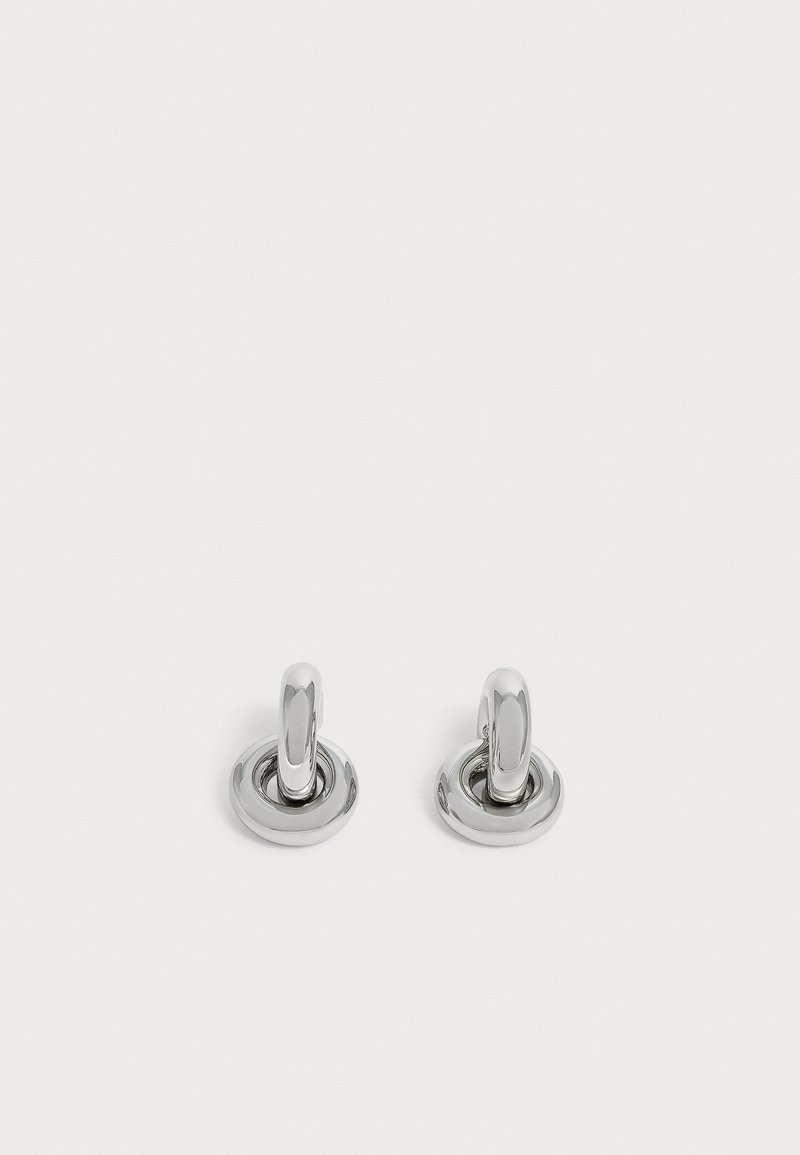 Paire de petites boucles d'oreilles créoles argentées brillantes avec une base ronde, présentées sur un fond clair uni.