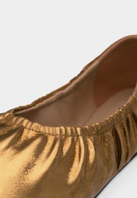 Κοντινό πλάνο ενός χρυσού μεταλλικού μπαλαρίνα παπουτσιού με μαζεμένα ελαστικά άκρα και απαλό, λείο εσωτερικό επένδυση.