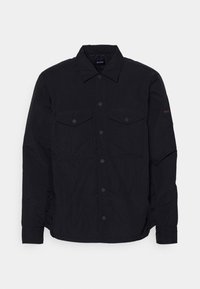 Černá košile na knoflíky z lehké látky. Má dvě náprsní kapsy, límec a jemné logo na rukávu. Strukturální povrch.