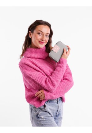 Pink knitted sweater with a high collar, paired with light denim jeans. The subject holds a grey wallet with a pink polka dot accent.