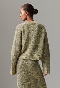 Camisola de malha em verde suave com acabamento texturizado em bouclé. Apresenta decote redondo e punhos canelados, combinada com uma saia a condizer.