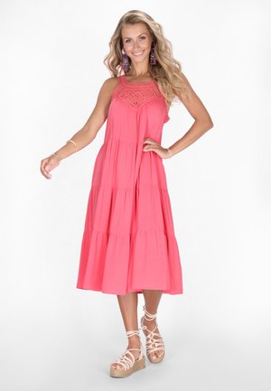 Korallenfarbiges, mehrstufiges Maxikleid mit Spitzenrand am Oberteil, dünnen Trägern und fließender Silhouette. Kombiniert mit hellbraunen Keilsandaletten.