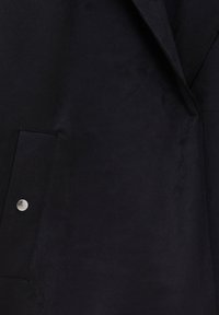 Black suede coat featuring a lapel collar, side pocket with silver snap button detail, and smooth, textured fabric.