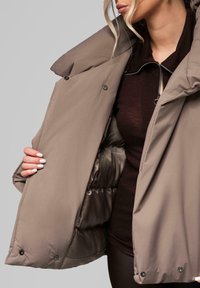 Tan puffer jacket with a high collar, zippered front, and snap buttons. Soft textured lining visible inside, featuring a quilted pattern.