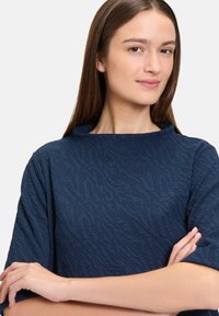 Granatowy pulower o teksturze z wysokim kołnierzem, krótkimi rękawami i luźnym krojem. Materiał charakteryzuje się subtelnie wzorowaną teksturą.