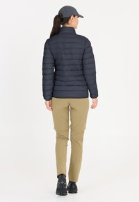 Marinblå puffjacka med horisontellt kviltat mönster, hög krage, i kombination med khaki-byxor och svarta vandringskängor, sedd bakifrån.
