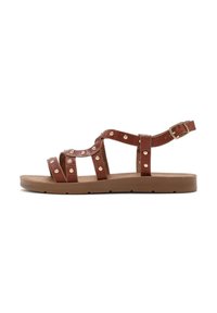 Brown leather sandals featuring multiple straps with gold studs, open sides, and an adjustable ankle buckle. Flat sole with minimal tread.