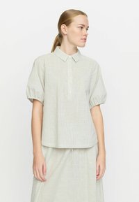 Camicia a maniche corte a righe in verde chiaro e bianco. Caratterizzata da un colletto, chiusura frontale con bottoni e un fitting rilassato con maniche arricciate.