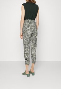 Spodnie w zielono-biały kwiatowy wzór o dopasowanym kroju, długości do kostek, zestawione z zielonymi klapkami na szerokim obcasie.