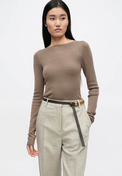 Smeđi rebrasti dolčevita s dugim rukavima u kombinaciji sa svijetlosivim krojenim hlačama i smešnim pojasom s zlatnim detaljima, na bijeloj pozadini.