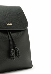 Mochila de cuero negro con un acabado texturizado, una solapa redondeada y un cierre de cordón con acentos anudados. Presenta un logo en dorado.