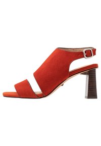 Sandały na podwyższeniu s otevřenou špičkou a páskem na patě v jasně červené semišové barvě. Mají blokový podpatek a dva široké pásky přes nohu s stříbrnou sponou.