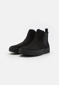 Black suede Chelsea boots with a textured rubber sole and elastic side panels for easy fit. Minimalist design, no visible hardware or patterns.