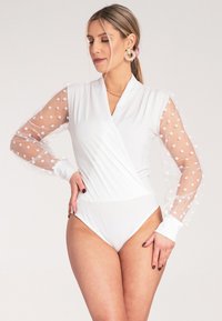 Biała bodówka o kroju z owijanym wzorem, z przezroczystymi rękawami w kropki i dopasowaną sylwetką. Gładka tkanina i kontrastujące teksturowane akcenty.