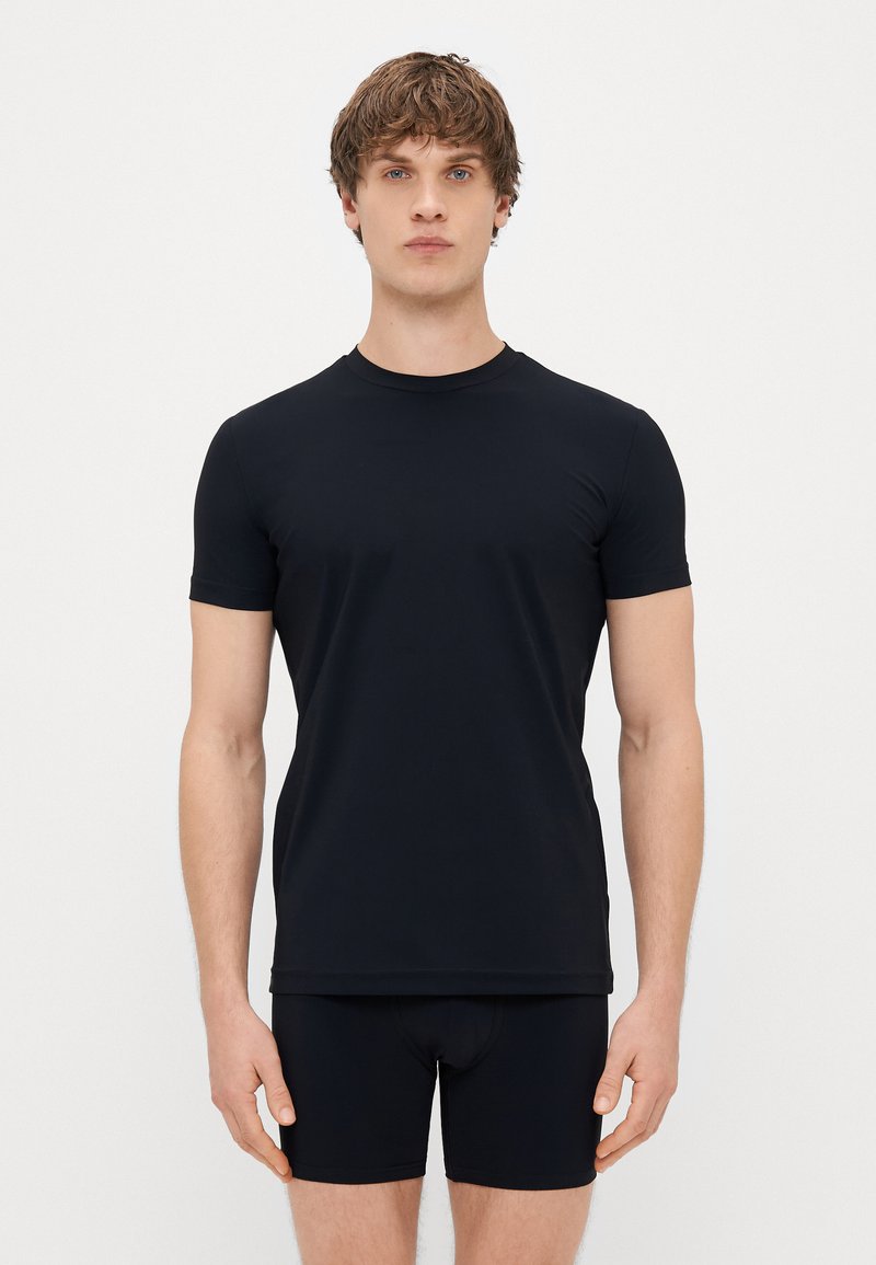 T-shirt nero a maniche corte realizzato in tessuto liscio e elastico. Design semplice con scollo a girocollo, silhouette aderente, abbinato a boxer neri.