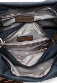 Intérieur d'un sac en tissu foncé avec plusieurs compartiments zippés, doublure gris clair imprimée de logos circulaires blancs et étiquettes de marque en cuir brun.
