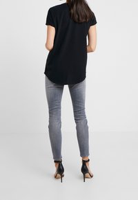 Svart kortärmad topp med rundad nederkant, tillsammans med ljusgrå skinny jeans och svarta högklackade skor. Enkel och figurnära design.