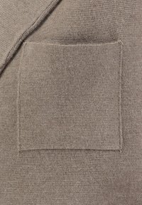 Beige gebreide trui stof met een vierkante zak. De textuur is glad met een fijne brei en minimale zichtbare naden.