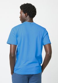 Kurzärmliges blaues T-Shirt aus Baumwolle, mit Rundhalsausschnitt, glatter Textur und einem kleinen Detail im Nackenbereich auf der Rückseite.