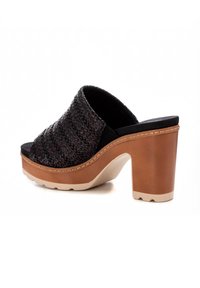 Sandalia plana trenzada negra con punta redondeada, tacón grueso color tostado y suela de color claro. Presenta un upper texturizado y un forro suave.