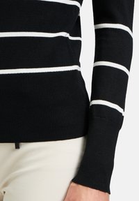 Schwarz gestreifter Pullover mit horizontalen weißen Streifen, gerippter Textur, taillierter Passform und Nahaufnahme des Bündchens und Saums.
