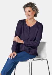 Blusa a maniche lunghe di colore blu navy con scollatura rotonda e chiusura a bottoni. Tessuto morbido e liscio con pieghe sottili e vestibilità rilassata.