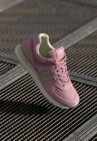 Rosa Sportschuh mit Obermaterial aus strukturiertem Stoff, hellgrünem Innenfutter und beige Akzenten. Verfügt über ein auffälliges "N"-Logo an der Seite.