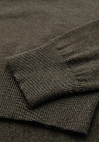 Tessuto di maglia verde scuro con polsini e orlo a coste. La texture appare liscia con una finitura morbida e elastica. Nessun motivo visibile.