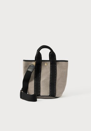 Petit sac fourre-tout en toile beige avec des poignées noires cousues, une bandoulière large noire amovible et un détail de bouton doré à l'avant.